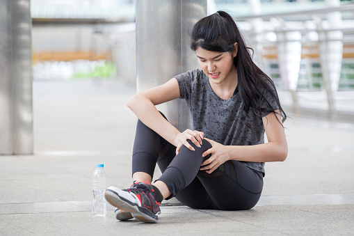 asian fitness young woman  Running injury leg accident  of workout exercising on street in urban city . sport runner girl sitting on floor holding knee in  pain